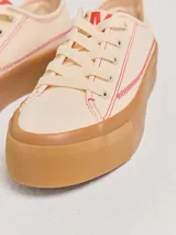 Championes bajos color crema con pespuntes rojos, capellada de tela canvas y plataforma de goma color caramelo de 4 cm de altura.