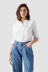 Camisa de vestir blanca de manga larga con cierre frontal de botones, cuello camisero y un bolsillo aplicado en el pecho con etiqueta roja característica.