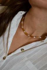 Collar tipo choker compuesto por cuentas cilíndricas de piedra color ámbar alternadas con pequeñas perlas blancas.