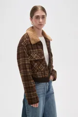 Campera corta de estilo bomber con estampado a cuadros en tonos marrones. Presenta cuello de corderito sintético, cierre frontal con cremallera, dos bolsillos frontales con solapa y puños y ruedo de tejido elástico acanalado.