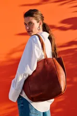 Cartera tipo shopper de cuero color terracota, sin forro y con terminaciones al corte. Cuenta con bolsillo interior con cierre.