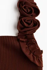 Top corto en punto fino acanalado de color marrón, con escote recto y breteles anchos con ribete de volados, uno de ellos decorado con apliques de rosas de tela.