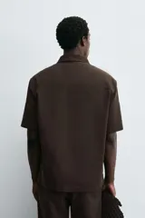 Camisa tipo polo de corte relajado confeccionada en una mezcla de lyocell y algodón. Presenta cuello con solapa, cierre frontal de botones ocultos, manga corta y un bolsillo de parche en el pecho. El bajo cuenta con aberturas laterales.