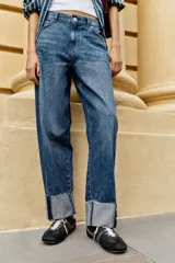 Jeans baggy de tiro medio con pernera holgada, diseño de cinco bolsillos y bajo acabado en vuelta. Cuenta con cintura elástica en la espalda y cierre frontal con cremallera y botón.