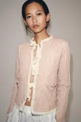 Chaqueta de punto color rosado con cuello redondo, manga larga y bolsillos delanteros. Presenta detalles de acabados con tejido combinado deshilachado en color blanco crudo y cierre frontal con lazos del mismo tono.