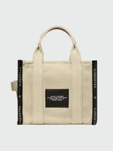 Bolso tipo tote de Marc Jacobs, confeccionado en tejido jacquard negro con detalles en color crema. Presenta el nombre del modelo estampado en el frente, doble asa superior y correa ajustable extraíble.