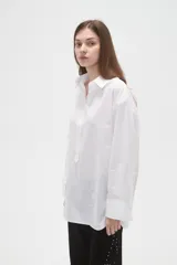 Camisa de algodón blanca de corte holgado, con cuello clásico, cierre frontal parcial con botones y mangas largas con puños anchos.