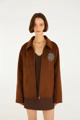 Campera de calce relajado color marrón, con cuello amplio, cierre frontal y mangas largas, confeccionada en tejido de acabado gamuzado con un parche bordado en el pecho.