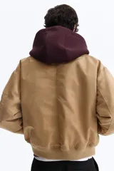 Campera bomber de nylon color tostado, con cuello, puños y bajo acanalados. Presenta cierre frontal, bolsillos laterales con botón a presión y un bolsillo con cierre en la manga.