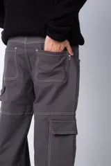 Pantalón tipo carpintero de corte relaxed fit y tiro medio, confeccionado en denim negro con costuras a contracolor en blanco. Presenta múltiples bolsillos cargo laterales, un bolsillo con cierre en la parte inferior y presillas utilitarias.