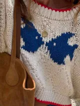 Sweater de tejido de punto grueso en color crema, con diseño de mariposas en color azul y detalles de terminación en color rojo en el cuello, puños y ruedo. Presenta un calce relajado, escote amplio y mangas largas.