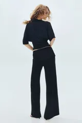 Pantalón negro de punto fino suave con piernas amplias y tiro alto. Presenta una cintura ancha con costuras laterales fruncidas para crear un efecto drapeado.