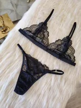 Conjunto de lencería compuesto por un bralette de encaje con breteles regulables y una tanga regulable con corte cola less. Ambas piezas presentan un diseño de encaje floral negro.