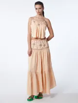 Conjunto de top corto y falda larga color durazno, con bordados florales en tonos marrones. El top tiene escote en pico y tirantes finos. La falda es de corte amplio y tiene volantes en el ruedo.