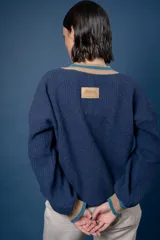Buzo de punto en color azul marino con escote en V, puños y cuello con detalles en franjas de color turquesa y rojo. Presenta un diseño holgado de manga larga.