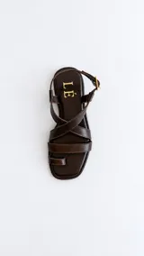Sandalias de cuero color marrón con diseño de tiras cruzadas en el empeine, sujetador para el dedo y tira ajustable con hebilla en el talón.