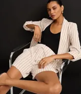 Blazer de poliéster color crudo con rayas verticales finas en marrón. Tiene cuello con solapas peaked, bolsillos delanteros y mangas largas con botón para arremangar. Sin forro.