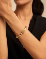 Pulsera rígida abierta bañada en oro, con diseño que simula un clavo, terminando en punta en un extremo y en forma de cabeza de clavo redonda en el otro.