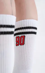 Medias 3/4 de algodón color blanco, con dos rayas negras horizontales en la parte superior y el número 90 bordado en color rojo con contorno negro.
