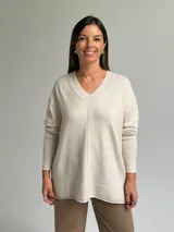Sweater de punto color beige con escote en V, diseño holgado y costura central vertical. Presenta mangas largas con puños acanalados y ruedo con terminación acanalada.
