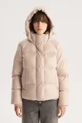 Campera puffer corta color beige con capucha desmontable, cierre frontal con cremallera y botones a presión, y cordón ajustable en el ruedo. Diseño acolchado con bolsillos laterales.