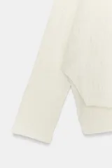 Jersey de punto con textura, color crudo, de cuello subido y manga larga. Presenta un diseño holgado con bajo asimétrico y aberturas laterales.