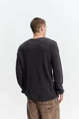Sweater oversize de tejido liviano color gris claro, con hombros caídos, cuello redondo, costuras a la vista y bordado sutil en el pecho.