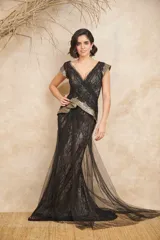 Vestido largo de encaje negro con capas de tul, escote en V cruzado, mangas cortas con detalles metalizados en dorado y falda de corte sirena con cola y sobrefalda drapeada.