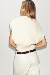 Chaleco de punto liso con escote en pico y diseño sin mangas. Presenta un corte corto con acabados en rib en el cuello, las sisas y el ruedo.
