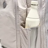 Mochila deportiva color gris, confeccionada en material textil con acabado arrugado. Presenta compartimento principal con cierre doble, bolsillo frontal con logo circular, compartimento inferior independiente para calzado y bolsillos laterales. Incluye tirantes ergonómicos ajustables y espaldera acolchada con malla transpirable.