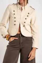 Chaqueta corta color beige de algodón, de inspiración militar con cuello mao y doble botonadura frontal con botones metálicos dorados.