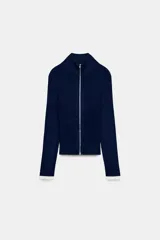 Chaqueta de punto acanalado azul marino con cuello alto y cierre frontal de cremallera metálica. Cuenta con detalles de rib en color blanco en los puños de las mangas largas.