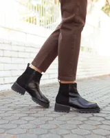 Botinetas de cuero negro con paneles laterales de gamuza al tono. Presentan una suela track robusta con taco cuadrado y cierre lateral para facilitar el calce.