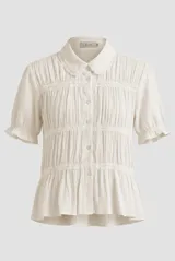 Camisa de lino color marfil con textura, cuello solapa redondo con detalles de encaje, mangas cortas abullonadas y franjas horizontales de puntilla.