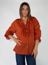 Blusa de manga larga color marrón, con cierre frontal de botones, escote en V y detalles de volados fruncidos alrededor del cuello y los puños elásticos.