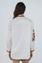 Camisa de algodón color blanco, de corte clásico con cuello camisero, manga larga y cierre frontal abotonado. Presenta un estampado tropical con palmeras y tigres, y detalles de ribetes a rayas en el cuello, la botonadura y los puños.