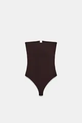 Body de tejido elástico color negro, con diseño strapless, escote recto con abertura frontal y cierre inferior con botones a presión.