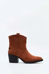 Bota corta de gamuza color marrón, de estilo texano, con taco cuadrado y punta fina. Cuenta con costuras decorativas y tirador lateral.