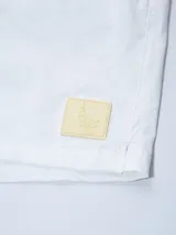 Short de baño blanco con cintura elástica y cordón ajustable. Tiene un parche cuadrado de color beige claro en la pierna izquierda.