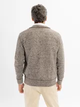 Campera tejida de punto jaspeado en tono azul, con cierre frontal completo, cuello alto y detalles de ribete en color marrón en los bolsillos y a lo largo del cierre. Presenta puños y ruedo acanalados.