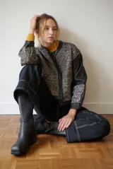Chaqueta de diseño combinado con paneles de tejido de espiga en tonos marrones y burdeos, y paneles de cuero marrón en mangas y bordes. Presenta cuello redondo, cierre frontal con botones metálicos a presión y bolsillos delanteros.