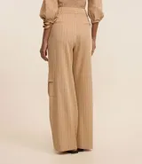 Pantalón wide leg de poliéster y elastano color beige con rayas verticales finas. Tiene corte de sastrería, doble trabilla en la cintura, bolsillos cargo laterales y cierre delantero.
