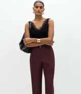 Pantalón carrot sastrero de corte recto y cintura alta, confeccionado en crepé. Presenta trabillas en la cintura, cierre tradicional y bolsillos traseros decorativos. Incluye un cinturón fino de material sintético.