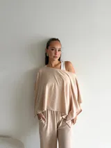 Conjunto de dos piezas compuesto por un top de corte asimétrico con escote amplio y mangas estilo capa, y un pantalón de corte recto y holgado. Ambas prendas están confeccionadas en tejido de lanilla gris.