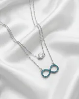 Collar doble de plata 925, compuesto por una cadena superior con dije de punto de luz y una cadena inferior con dije en forma de símbolo de infinito decorado con circonias turquesas.