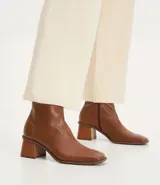 Bota de cuero de caña media para mujer, con punta cuadrada y tacón bloque de 6 cm. Presenta un cierre de cremallera en el lateral interno y una costura central decorativa en la parte frontal.