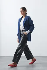 Pantalón de tiro medio en símil cuero color negro, con corte flare, bolsillos laterales y costuras frontales verticales que estilizan la silueta.