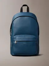 Mochila Calvin Klein de poliuretano texturizado en color azul, con compartimento principal con cierre de doble cremallera, bolsillo frontal con cierre, asa superior y tirantes ajustables. Incluye detalle de logo metálico de la marca en el frente.