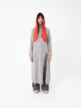 Buzo largo gris de tejido de punto grueso con cuello alto y capucha con orejas de conejo rojas. Tiene mangas largas y un tajo lateral.