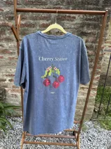 Remera de algodón con efecto lavado, manga corta y estampa frontal con diseño de cerezas pixeladas y texto Cherry Season.